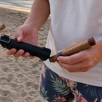 Man on a beach using the punch tip in the TacFlame base on a cigar