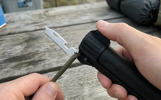 Folding knife out of the TacFlame lower handle cutting paracord on a picnic table