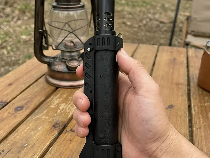 Hand holding the TacFlame torch on a wooden camp table, vintage lantern behind
