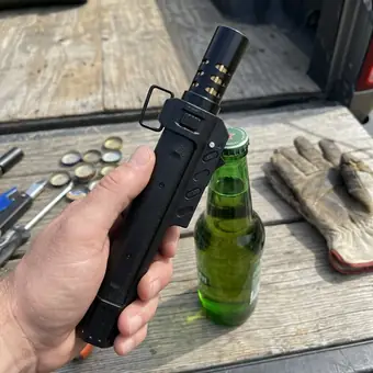 Hand holding a TacFlame on a tailgate with bottle caps, a beer bottle and work gloves