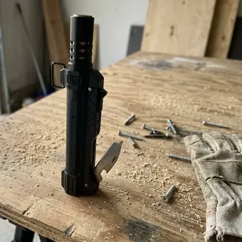 TacFlame standing on a dusty workbench with nails and gloves, folding knife out